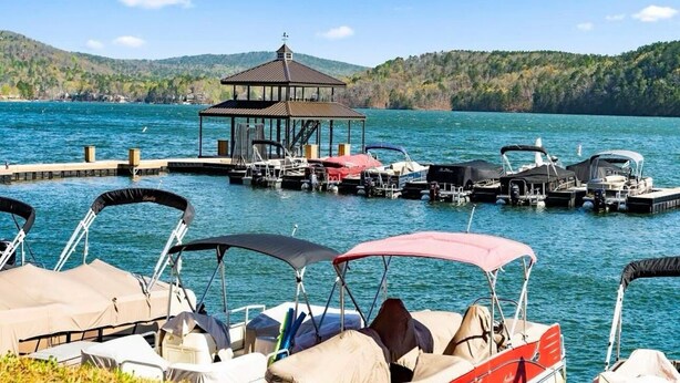Un muelle junto al lago con barcos, un pabellón cubierto y un promontorio boscoso al fondo.