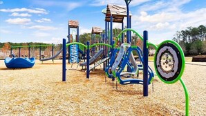Un patio de recreo con diversas estructuras de juego, incluyendo toboganes y zonas de escalada, sobre un suelo de madera.