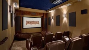 Una sala de cine en casa con techo estrellado, una pantalla grande mostrando "Grand Lodge" y sillones de cuero reclinables.