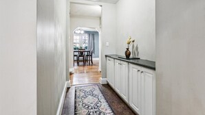 A hallway with white walls, a patterned rug, and a kitchen area with white cabinets and a countertop. - Family and dog friendly home, 30+ day stays (Norfolk)