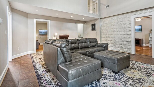 A spacious living room with a large sectional sofa and ottoman, a patterned rug, and a high ceiling with a balcony. - Family and dog friendly home, 30+ day stays (Norfolk)