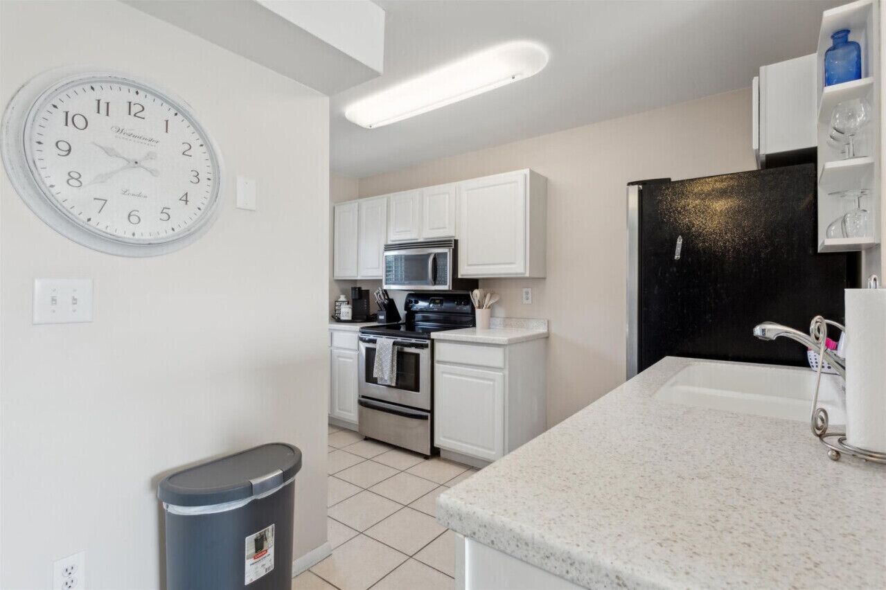 A modern kitchen with white cabinets, a black refrigerator, a microwave, and a stainless steel oven.