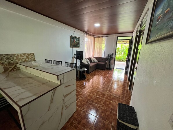 A compact living space with a kitchen area, a dining table, a sofa, and a fan.