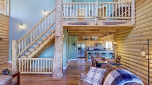 Ein Holzblockhaus-Interieur mit einer Holztreppe, einer Küchenzeile und einer gemütlichen Sitzecke mit einem karierten Überwurf.