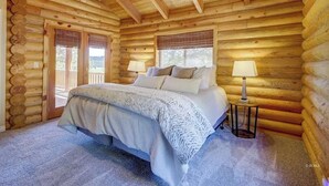Ein Schlafzimmer in einer Blockhütte mit einem Bett, zwei Nachttischlampen und einem Fenster.