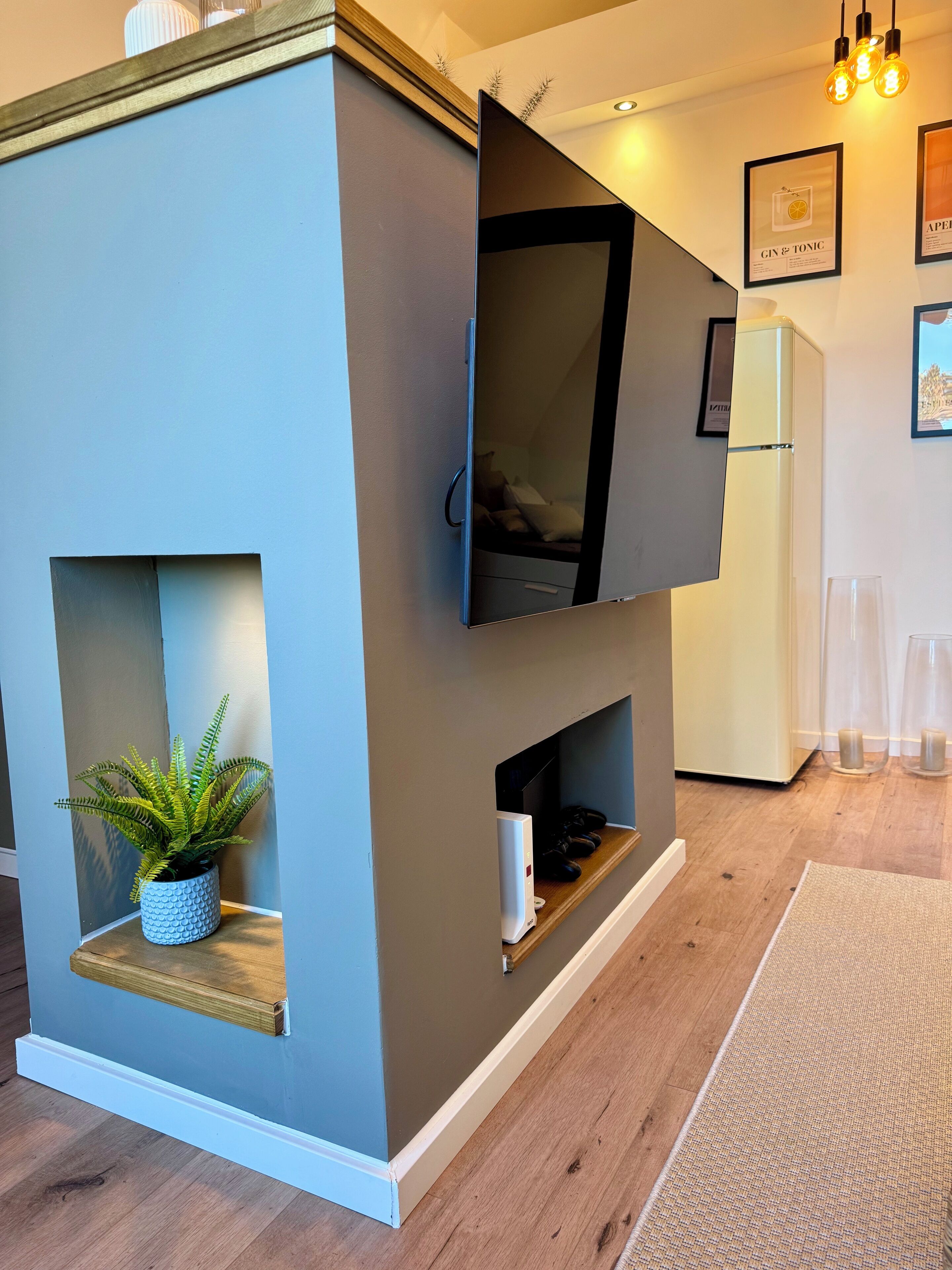 A modern living room with a built-in TV, a small plant, and a white refrigerator.
