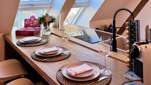 Un coin repas avec une table dressée pour quatre personnes, une machine à café et une vue sur l’extérieur grâce à des fenêtres de toit.