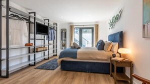 A modern bedroom with a bed, a TV, a wardrobe, and a view of the outdoors. - 4 Bed in Instow (oc-d30010) (Instow)