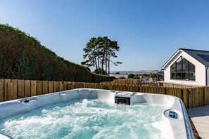 Un bain à remous entouré d’une clôture en bois, avec une maison en arrière-plan.
