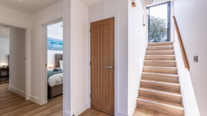 A modern interior with a wooden staircase, a wooden door, and a view of a bedroom with a bed and a window. - 4 Bed in Instow (oc-d30010) (Instow)