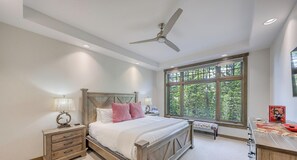 Une chambre à coucher comprenant un lit, des tables de chevet, un bureau, une fenêtre avec vue et un ventilateur de plafond.