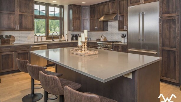 Una cocina moderna con armarios de madera oscura, una isla grande con taburetes de bar, un refrigerador de acero inoxidable y un ventanal con vistas al exterior.