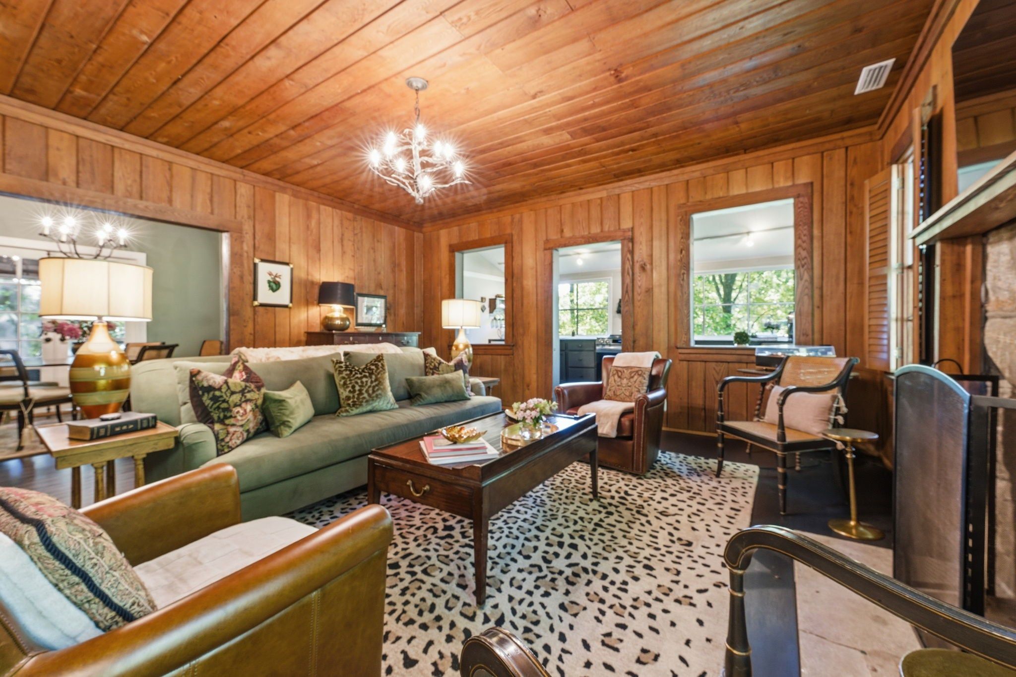 A cozy living room with wooden walls, a green sofa, leather chairs, a coffee table, and a patterned rug.