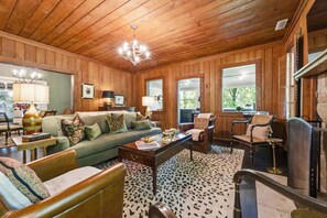 A cozy living room with wooden walls, a green sofa, leather chairs, a coffee table, and a patterned rug.