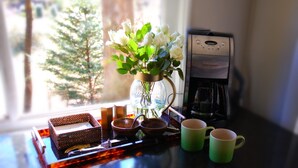 Une machine à café, un vase avec des fleurs et deux tasses sur une table près d’une fenêtre.