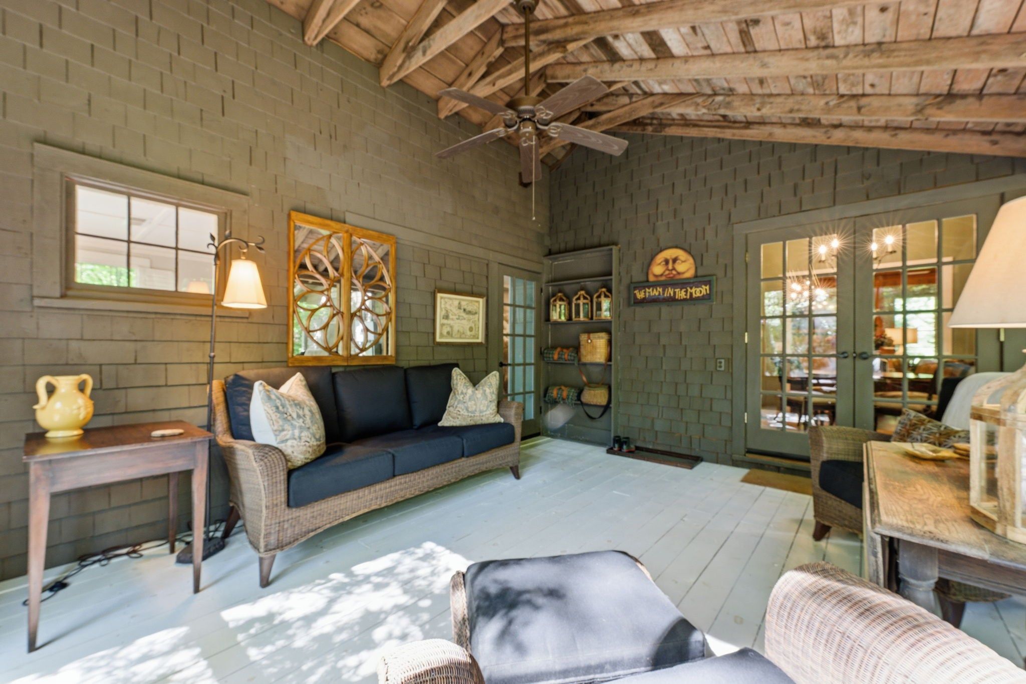 A cozy room with a wooden ceiling, a sofa set, a table with a lamp, and a wall with decorative items.
