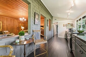 A kitchen with a wooden ceiling, a dining area with a table and chairs, and a view of the outdoors through large windows.