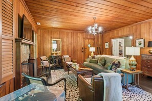 Una habitación con paredes y techo de madera, un sofá, una mesa de centro, una silla, una lámpara y un espejo.