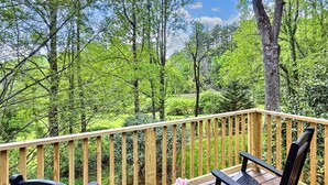 Une terrasse en bois avec deux chaises noires et une petite table, donnant sur une forêt verdoyante et luxuriante.