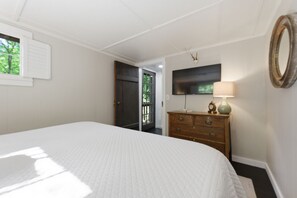 A bedroom with a large bed, a dresser, a television, and a door leading outside. - The Hideaway Of Horse Cove (Highlands)