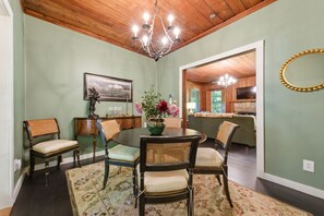 Une salle à manger avec une table ronde, des chaises, un lustre, un tableau et un vase rempli de fleurs.