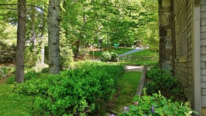 Un jardin résidentiel avec un chemin, une clôture en bois et une maison dont les murs sont recouverts de pierres.