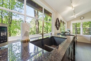 A kitchen with a large granite countertop, a stainless steel faucet, and a digital clock on the wall. - The Hideaway Of Horse Cove (Highlands)