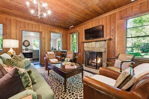 A cozy living room with a fireplace, wooden walls, and a view of the outdoors. - The Hideaway Of Horse Cove (Highlands)