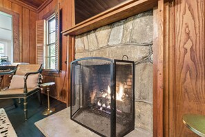Una chimenea de piedra con pantalla de vidrio, paredes de madera y un banco con cojines.