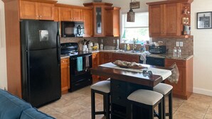 A modern kitchen with wooden cabinets, a black refrigerator, a microwave, and a stove. There is a dining table with bar stools. - Charming 2-bedroom house with WiFi, AC in delightful Key Largo (Key Largo)