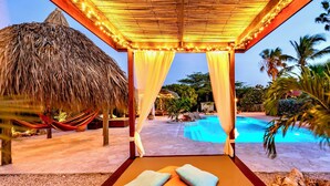A poolside lounge area with a thatched roof, a hammock, and a view of a swimming pool. - Luxury studio, oasis of peace, centrally located close to most beautiful beaches (Sint Willibrordus)