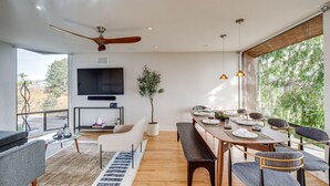 A modern living room with a large TV, a dining area with a wooden table, and a ceiling fan.