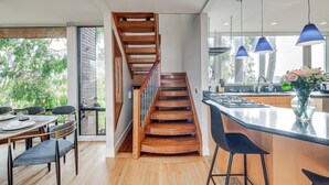 A modern kitchen with a wooden staircase, large windows, and a bar area.