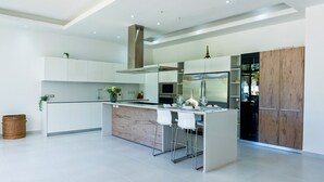 Una cuina moderna amb armaris blancs, electrodomèstics d'acer inoxidable i una illa central amb tamborets.