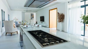 Una cuina moderna amb una illa central, una zona de menjador amb sofà i un gran finestral amb cortines.