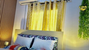 Un lit bien fait, avec une couvre-lit à motifs et des oreillers, une table de chevet avec une lampe et un climatiseur fixé au mur.