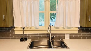 Una cocina con un lavaplatos doble, una ventana con cortinas y armarios de madera.