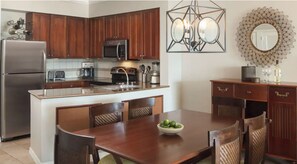 Una cocina con armarios de madera, electrodomésticos de acero inoxidable, una isla central con sillas y un espejo decorativo en la pared.