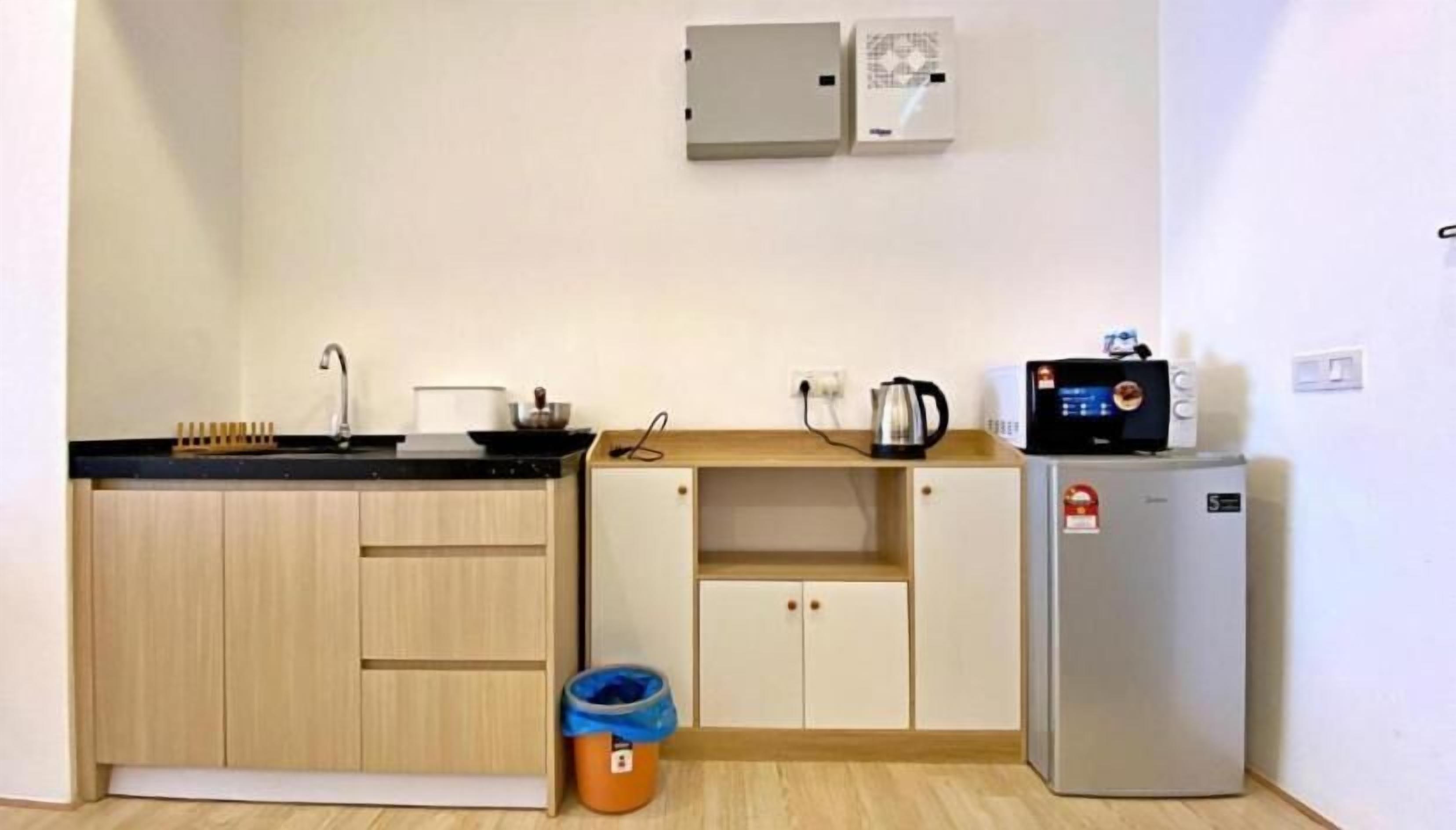 Una cocina compacta con un lavamanos, una tetera, un refrigerador pequeño y un cesto de basura.