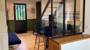 Een moderne keuken met een glazen scheiding, een eethoek met blauwe stoelen, en een trap die naar een verdieping leidt.