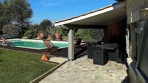 Een overdekt terras met een zwembad, tuinmeubilair en een verzorgd gazon.