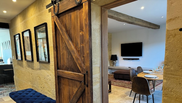 Een kamer met een houten deur, een blauwe bank, een eettafel gedekt met borden en glazen, en een flatscreen televisie aan de muur bevestigd.