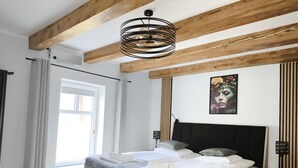 A modern bedroom with a large bed, wooden beams, a ceiling light, and a window. - Apartamenty Rynek Szamotuły (Szamotuly)