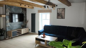 A modern living room with exposed wooden beams, a large flat-screen TV, a dark blue sofa, a coffee table, and a potted plant. - Apartamenty Rynek Szamotuły (Szamotuly)