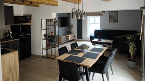 A modern kitchen with a dining area, wooden beams, a TV, and a sofa. - Apartamenty Rynek Szamotuły (Szamotuly)