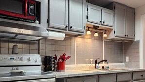 Une cuisine moderne avec des meubles gris, une hotte en acier inoxydable, un micro-ondes rouge et un four encastré.