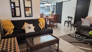 Un salon avec un canapé noir, une table basse et un coin repas comprenant une table et des chaises en bois.