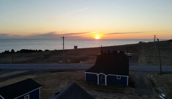 A coastal landscape with a sunset, a road, and a small building.