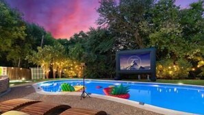 Una piscina con tumbonas de madera y una pantalla proyectando una imagen panorámica.