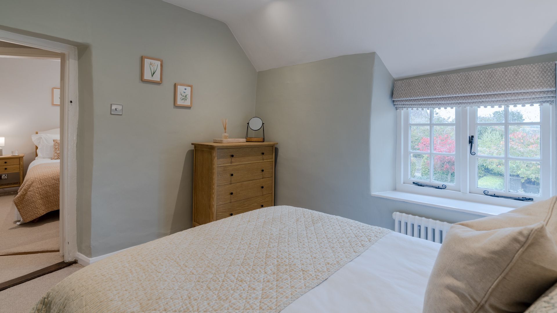 A bedroom with a bed, a dresser, a window with a view of trees, and a door leading to another room.
